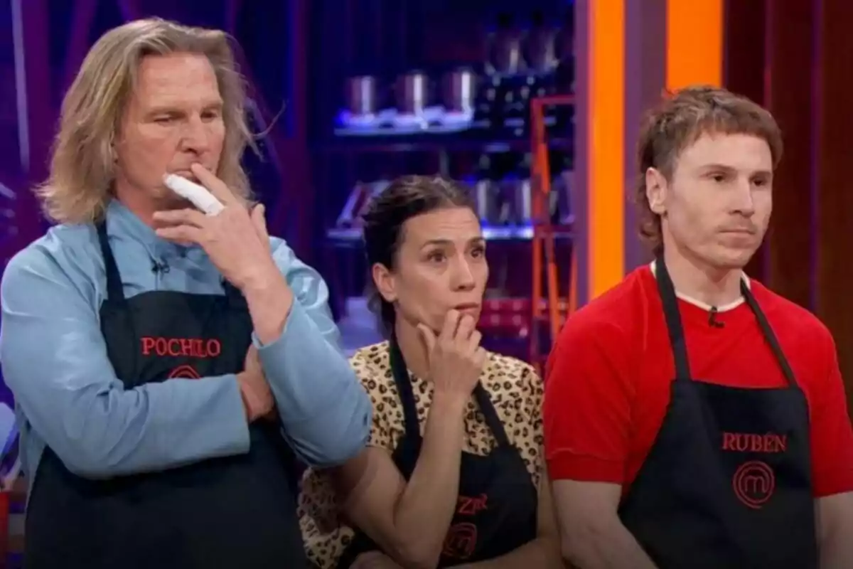 Pocholo Martínez Bordiú, Itziar Miranda y Rubén Ochandiano con delantales de cocina están de pie, mirando hacia adelante con expresiones serias y pensativas en MasterChef Celebrity.