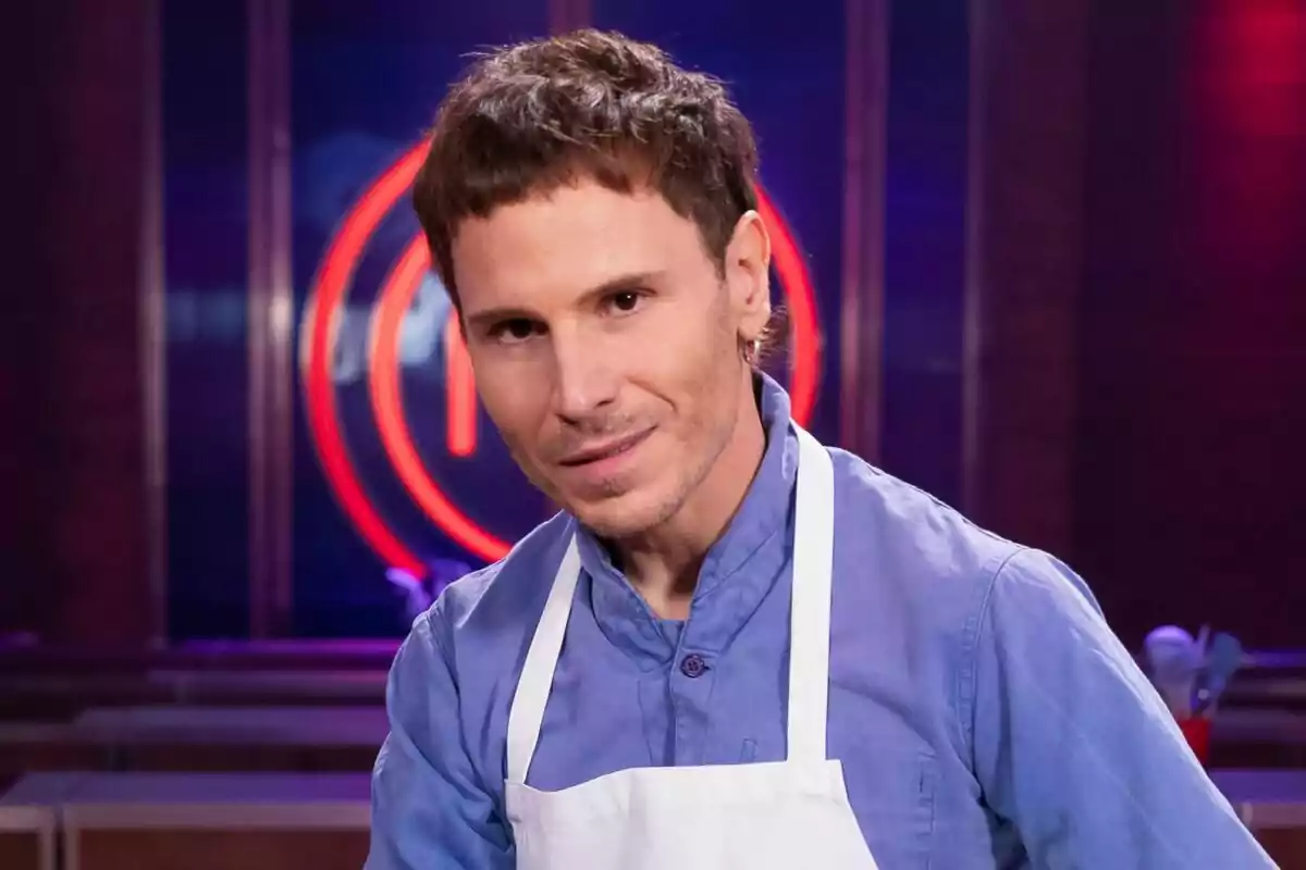 Rubén Ochandiano con delantal blanco y camisa azul en un set de cocina con un logotipo rojo de MasterChef Celebrity en el fondo.