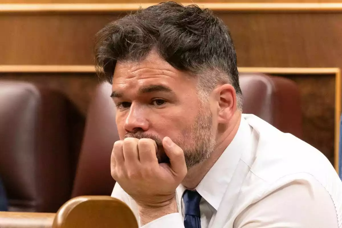 Gabriel Rufián con camisa blanca y corbata azul sentado en una sala, con la mano en la barbilla y expresión pensativa.