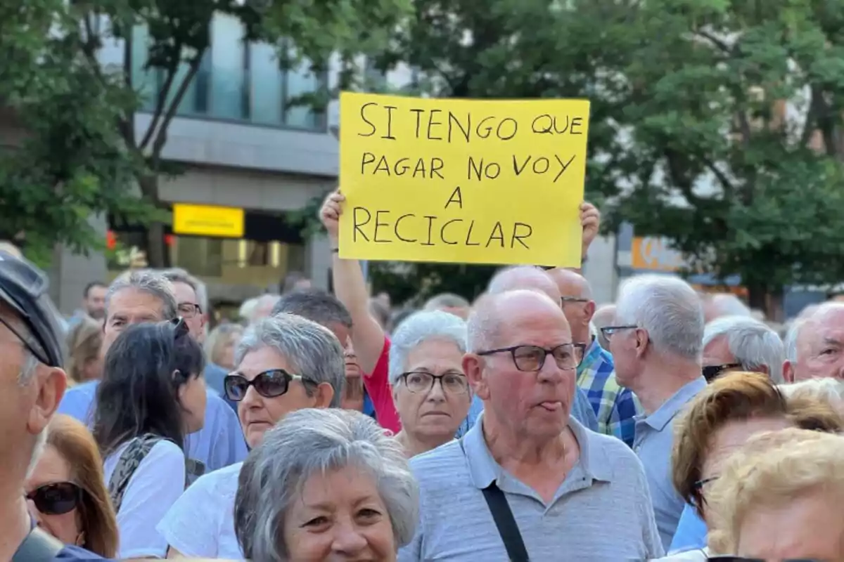 Imagen de centenares de vecinos de Sabadell manifestándose contra el aumento del impuesto de basura: un hombre lleva una pancarta con el lema 'si tengo que pagar no voy a reciclar'