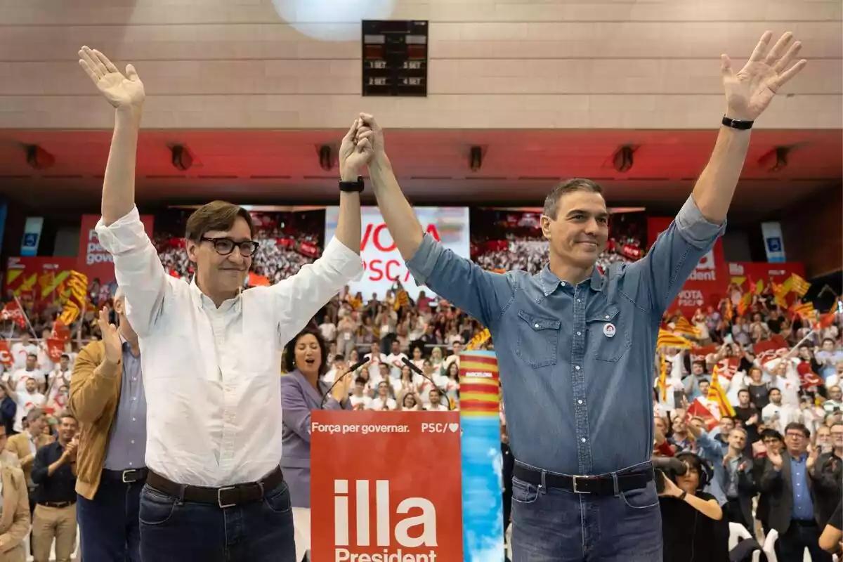 Salvador Illa y Pedro Sánchez agarrados de la mano con rostro sonriente en un acto del PSC