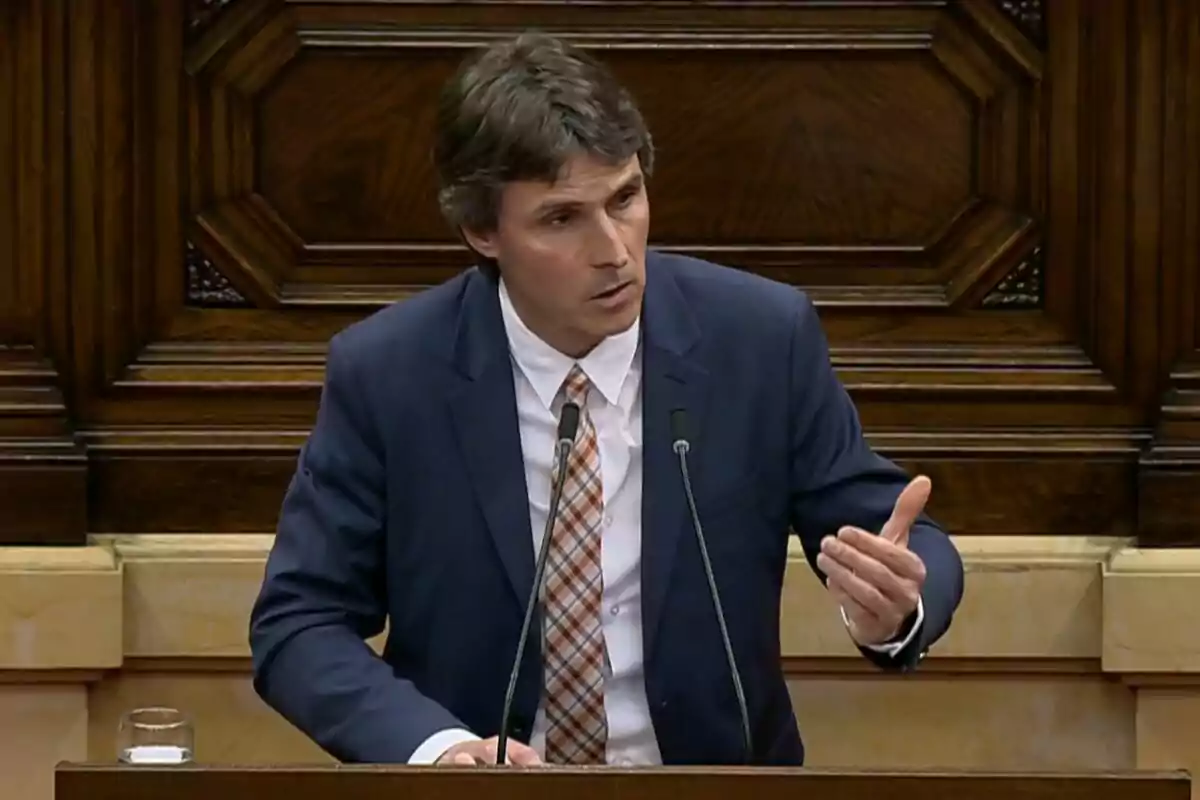 Un hombre en traje hablando en un podio con fondo de madera.