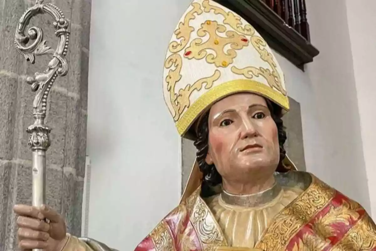 Una estatua de un obispo con mitra y báculo en el interior de una iglesia.