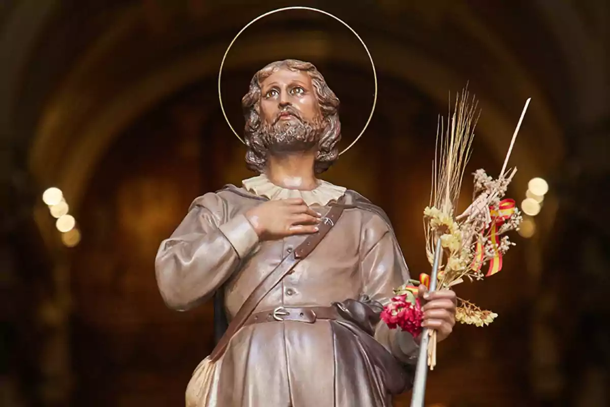 Una estatua de un hombre con aureola sosteniendo un ramo de flores y espigas.