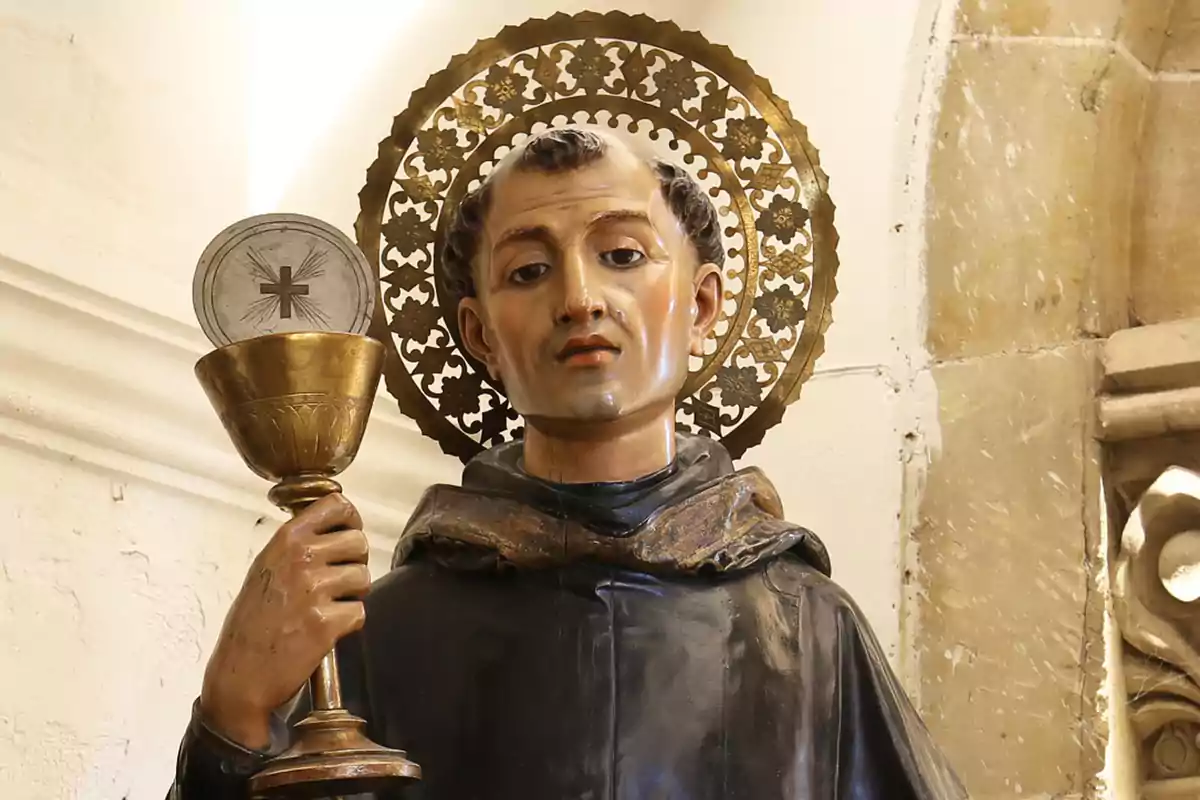 Escultura religiosa de un santo con aureola dorada sosteniendo un cáliz y una hostia