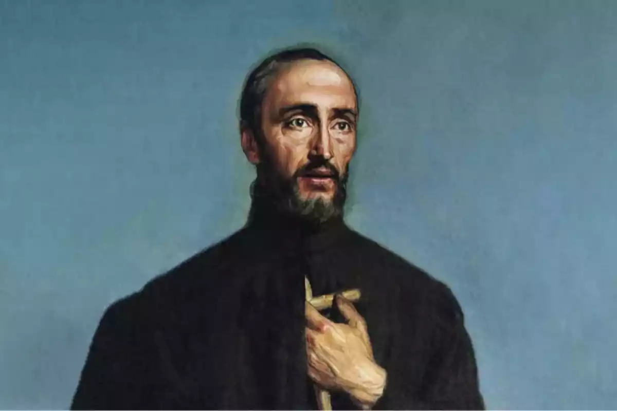 Retrato de un hombre con barba y cabello corto vestido con túnica negra sosteniendo una cruz de madera sobre el pecho frente a un fondo azul Retrato de un hombre con barba y cabello corto vestido con túnica negra sosteniendo una cruz de madera sobre el pecho frente a un fondo azul