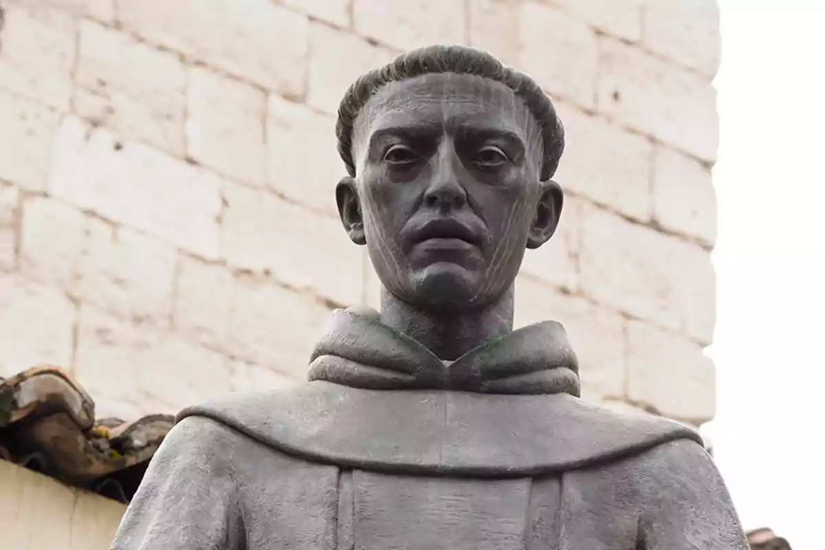 Una estatua de un monje con capucha frente a una pared de ladrillos. Una estatua de un monje con capucha frente a una pared de ladrillos.