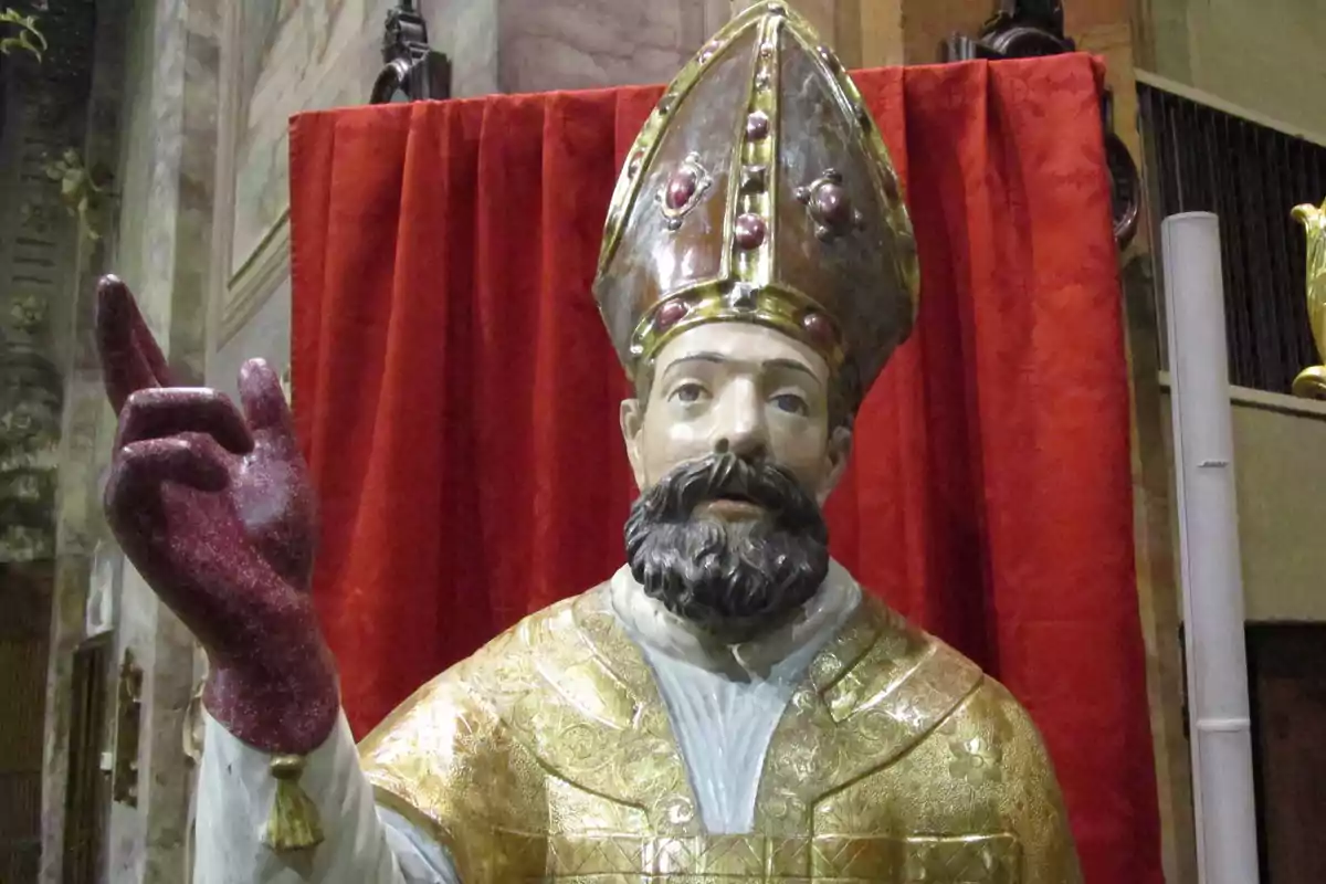 Escultura de un obispo con mitra y vestimenta dorada frente a un fondo rojo. Escultura de un obispo con mitra y vestimenta dorada frente a un fondo rojo.