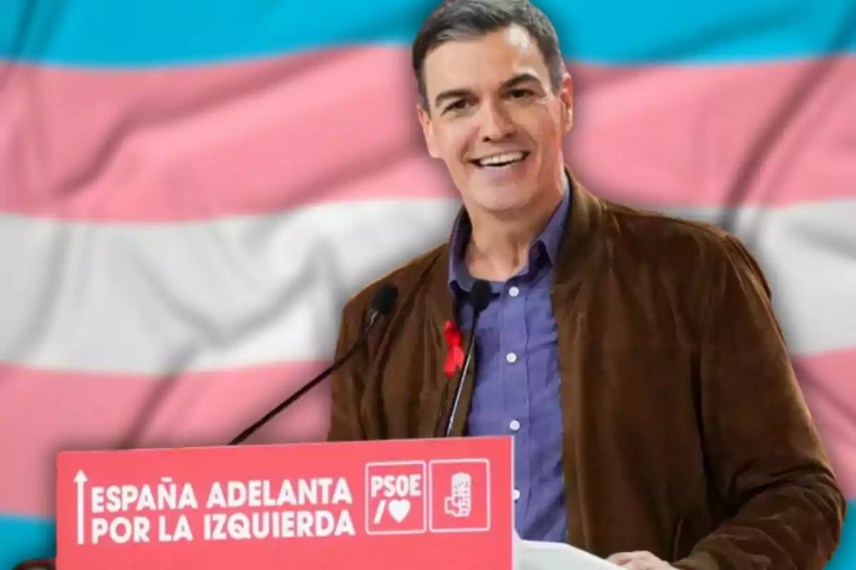 Un hombre sonriente en un podio con un cartel que dice "España adelanta por la izquierda" y el logo del PSOE, con una bandera de colores en el fondo.