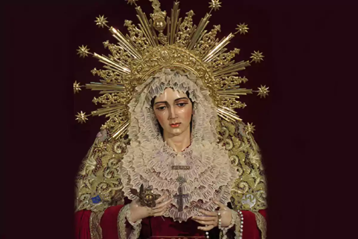 Imagen de una figura religiosa de la Virgen María vestida con manto bordado en dorado y tocado de encaje, con una corona dorada decorada con rayos y estrellas sobre un fondo oscuro Imagen de una figura religiosa de la Virgen María vestida con manto bordado en dorado y tocado de encaje, con una corona dorada decorada con rayos y estrellas sobre un fondo oscuro