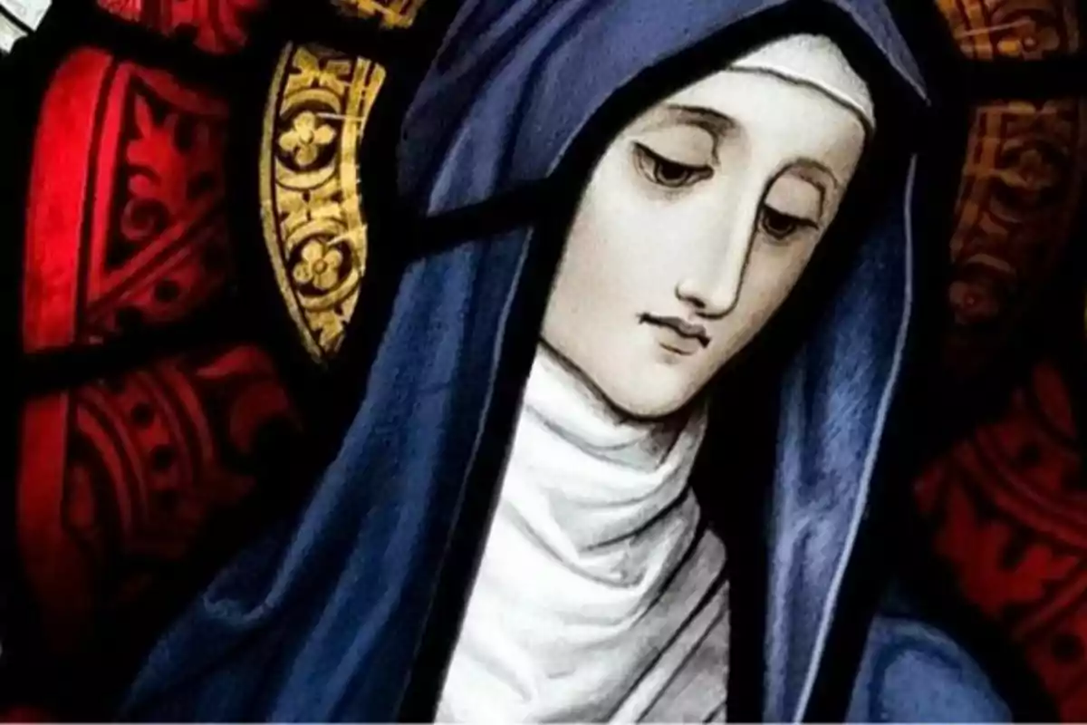 Imagen de un vitral que representa a una figura religiosa con manto azul y fondo decorativo en tonos rojos y dorados.