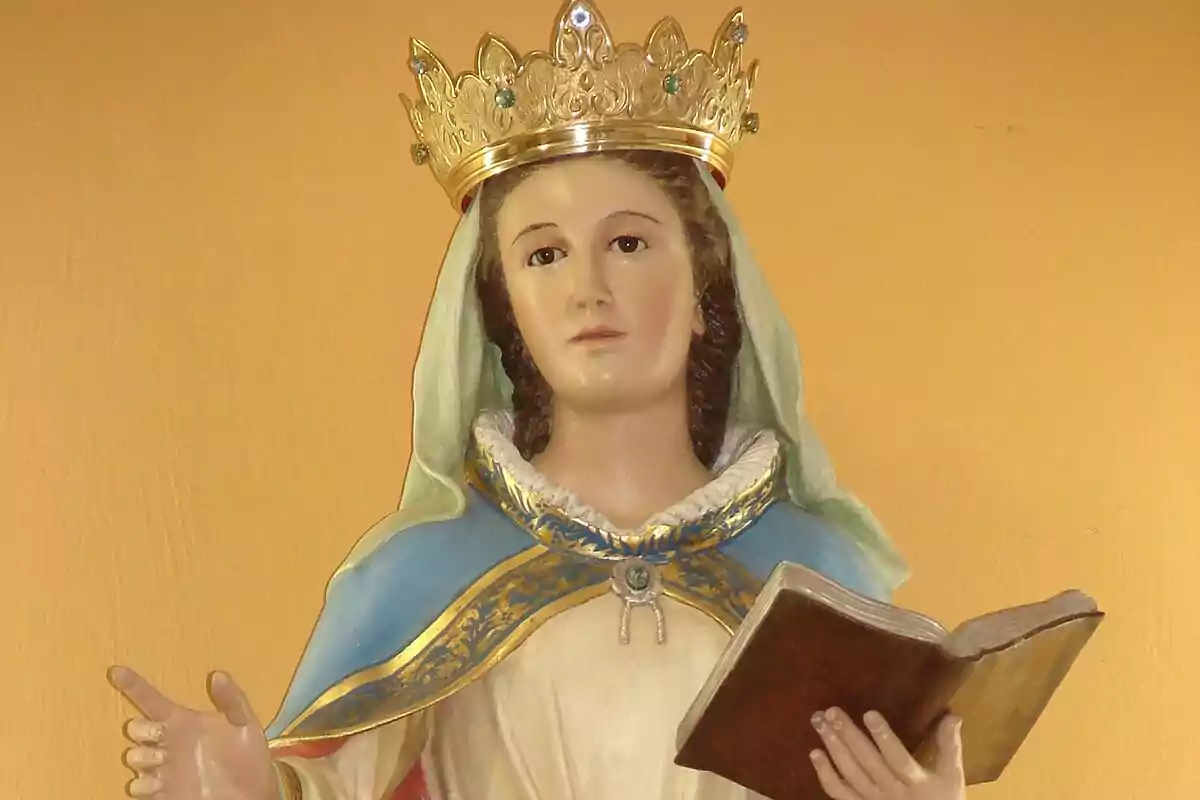 Estatua de una figura religiosa con corona y libro en la mano.