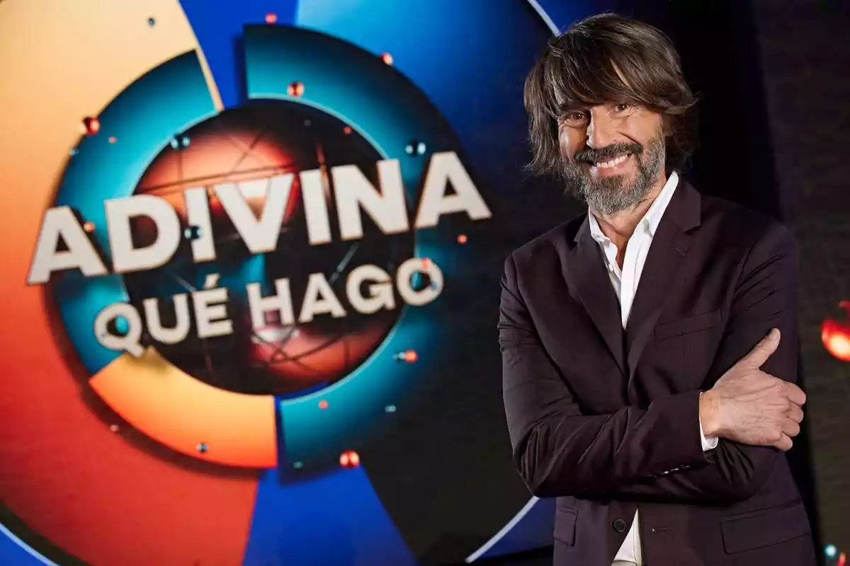 Fotografía de Santi Millán posando delante del logo de Adivina qué hago en Telecinco