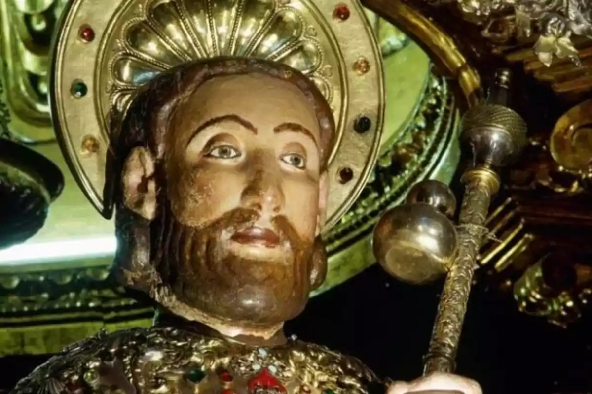 Estatua religiosa de un santo con aureola dorada y vestimenta adornada con joyas.