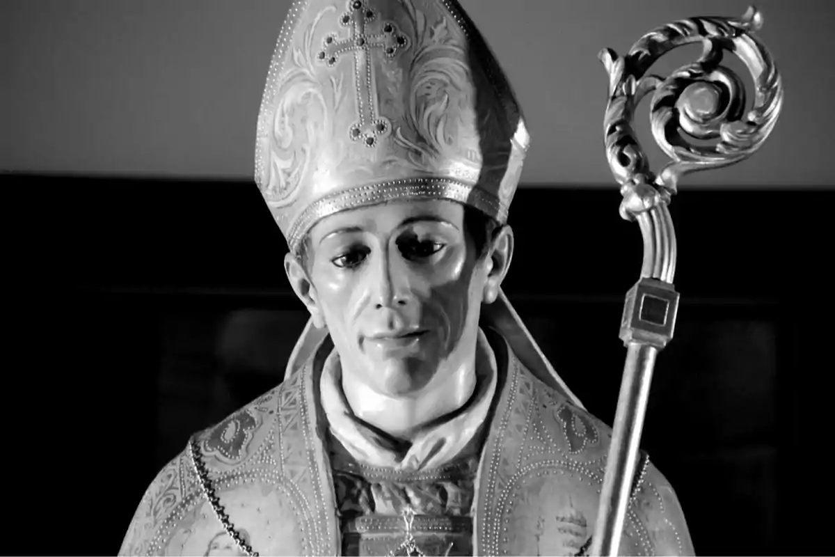 Escultura religiosa de un obispo con mitra y báculo en blanco y negro.