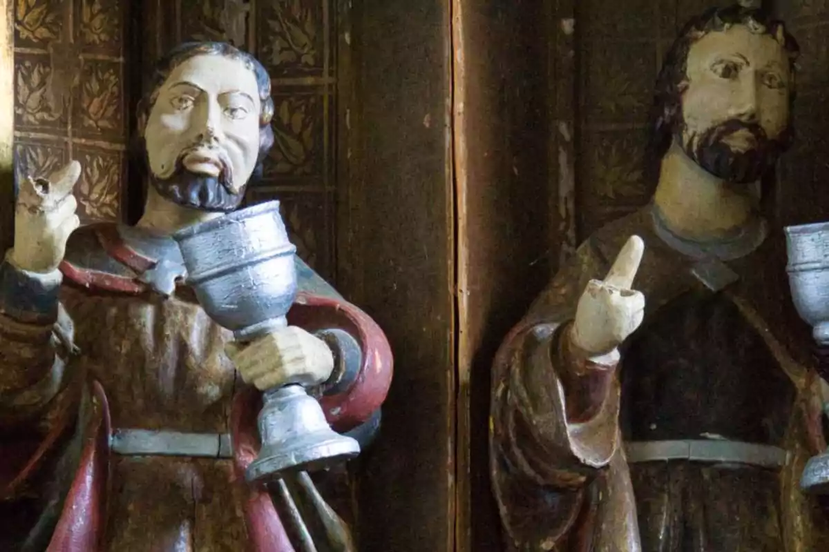 Dos figuras religiosas de madera sosteniendo copas con expresiones serias.