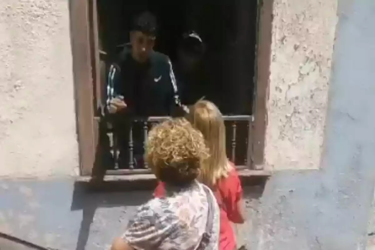 Dos personas están de pie frente a una ventana hablando con alguien que está adentro.