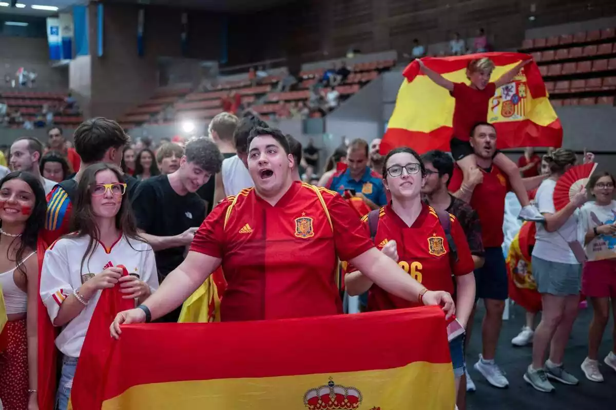 Varios aficionados de la selección española animan al equipo en un pavellón de la Vall d'Herbon, luciendo camisetas de la selección y banderas españolas