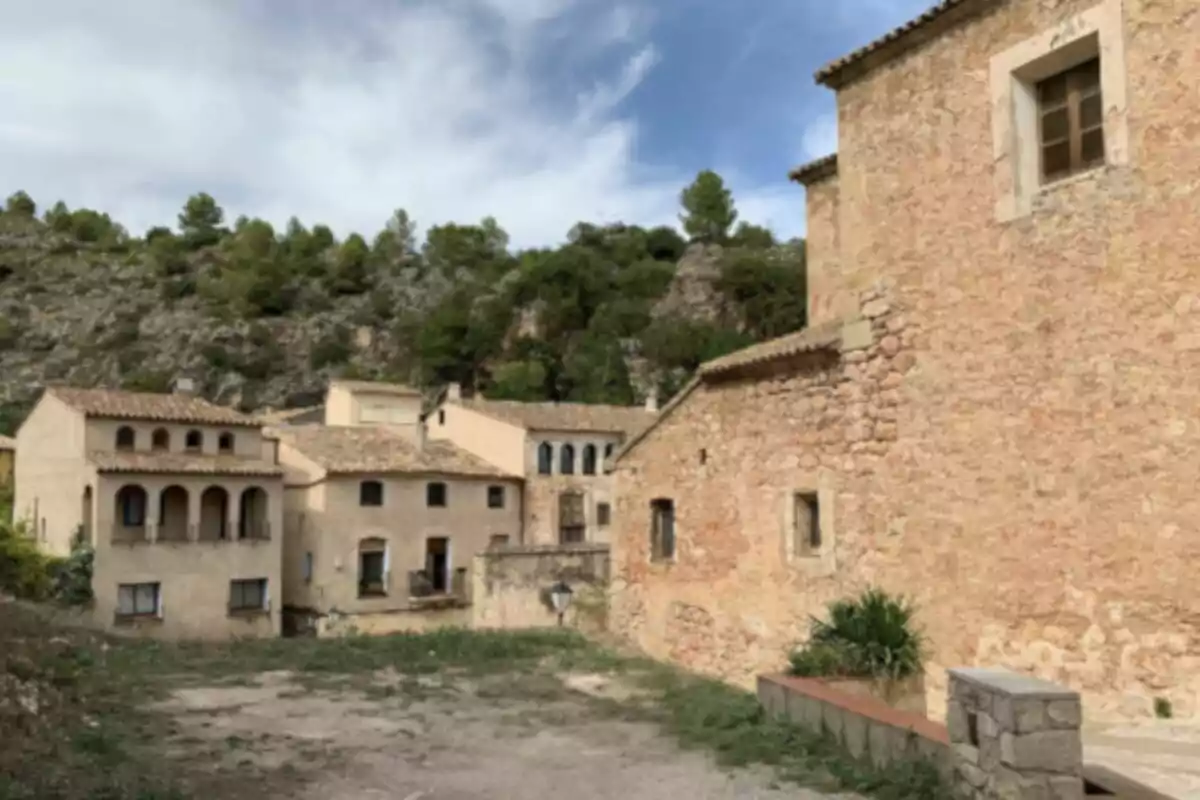 Un pequeño pueblo con casas de piedra y techos de teja rodeado de colinas y vegetación. Un pequeño pueblo con casas de piedra y techos de teja rodeado de colinas y vegetación.