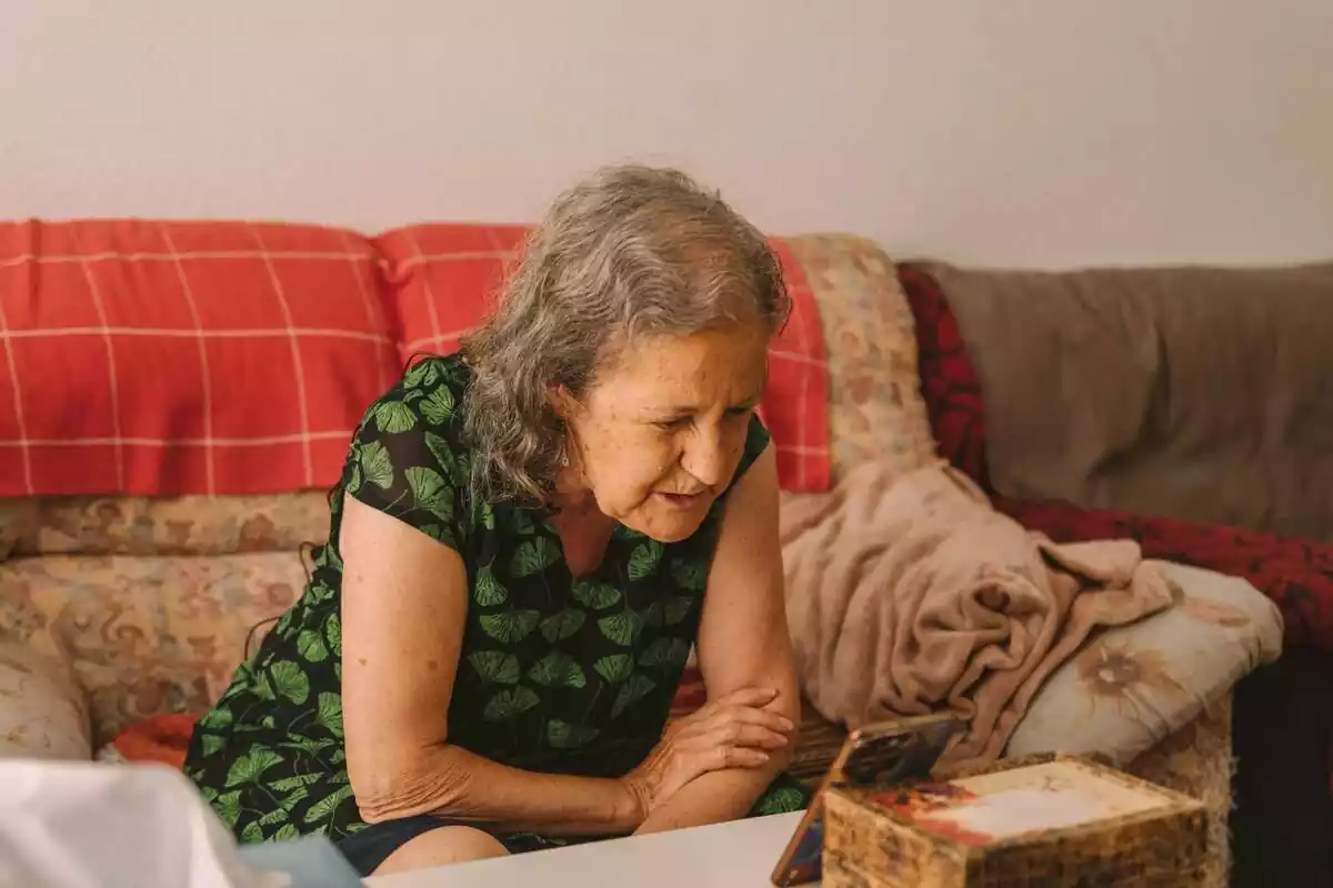 Imagen de una mujer mayor, sentada en un sofá, hablando con alguien a través de un móvil por videollamada