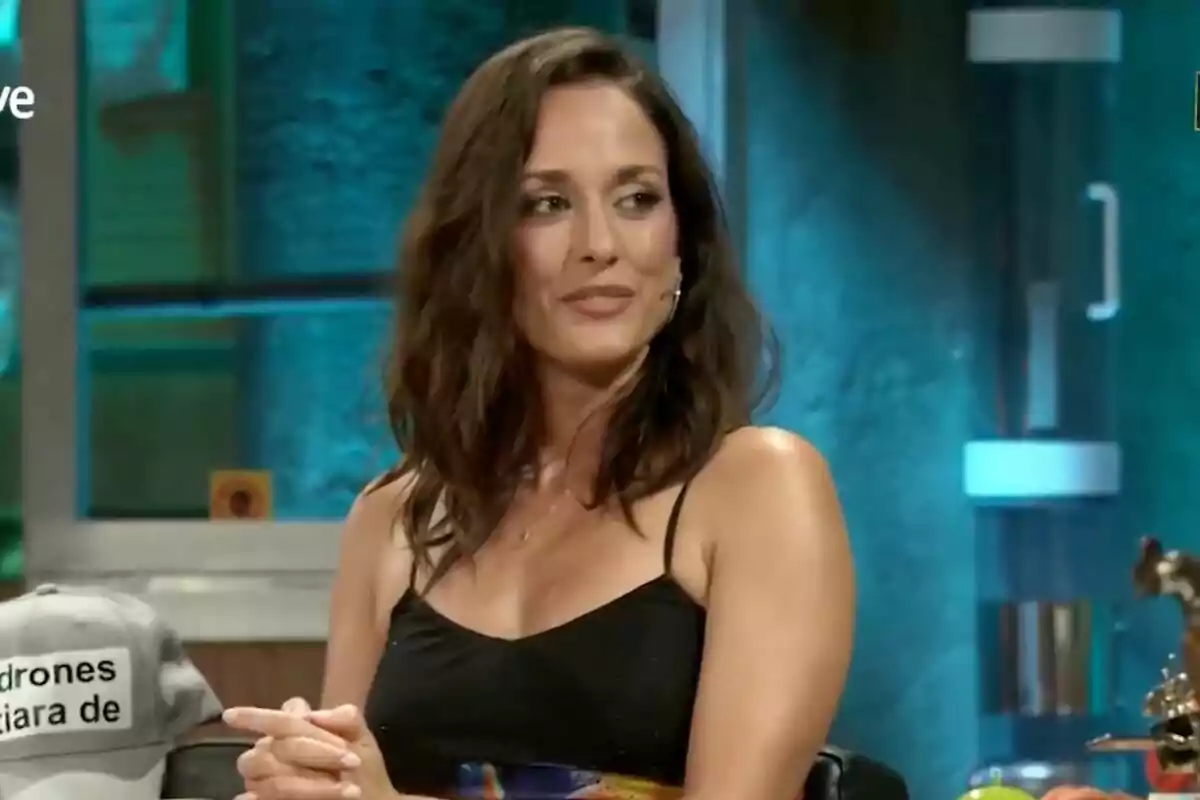 Silvia Alonso con cabello castaño y ondulado sentada en 'La Revuelta' con fondo azul y una gorra gris a su lado