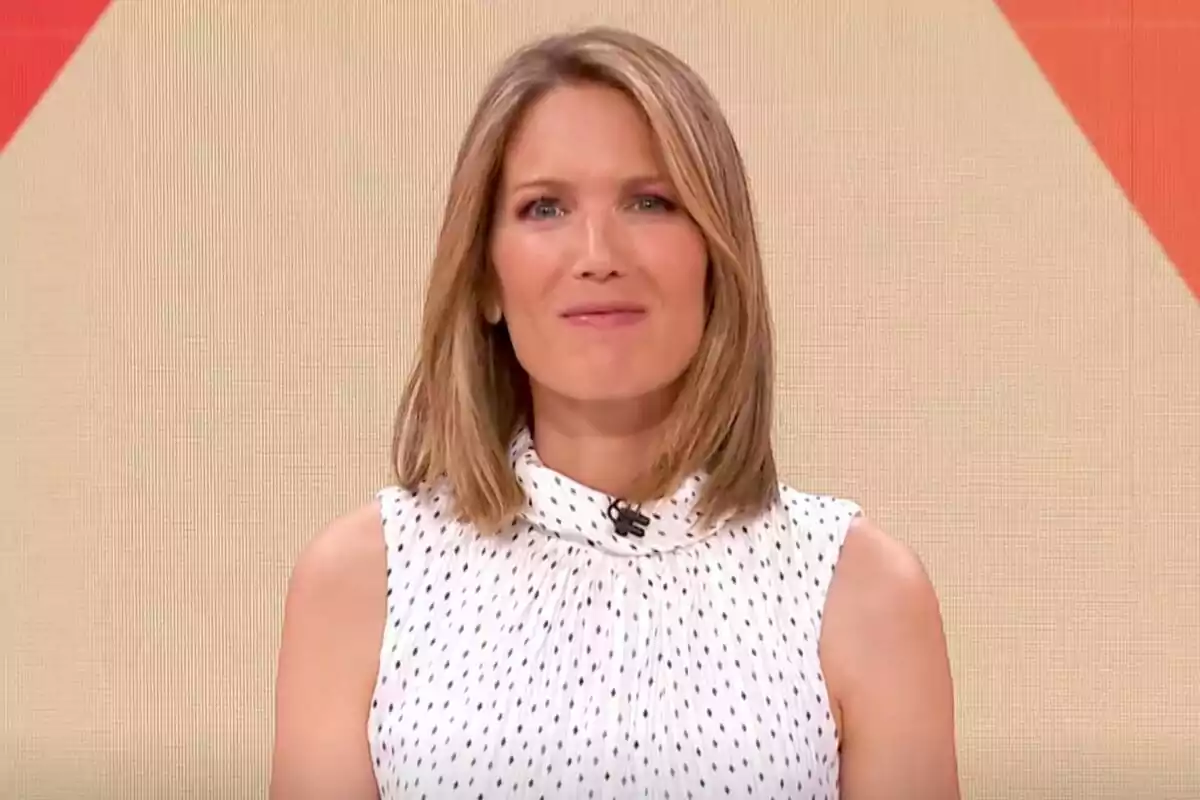 Captura de Silvia Intxaurrondo con cabello rubio y lacio, usando una blusa blanca con puntos negros, frente a un fondo beige con detalles en rojo en La Hora de La 1