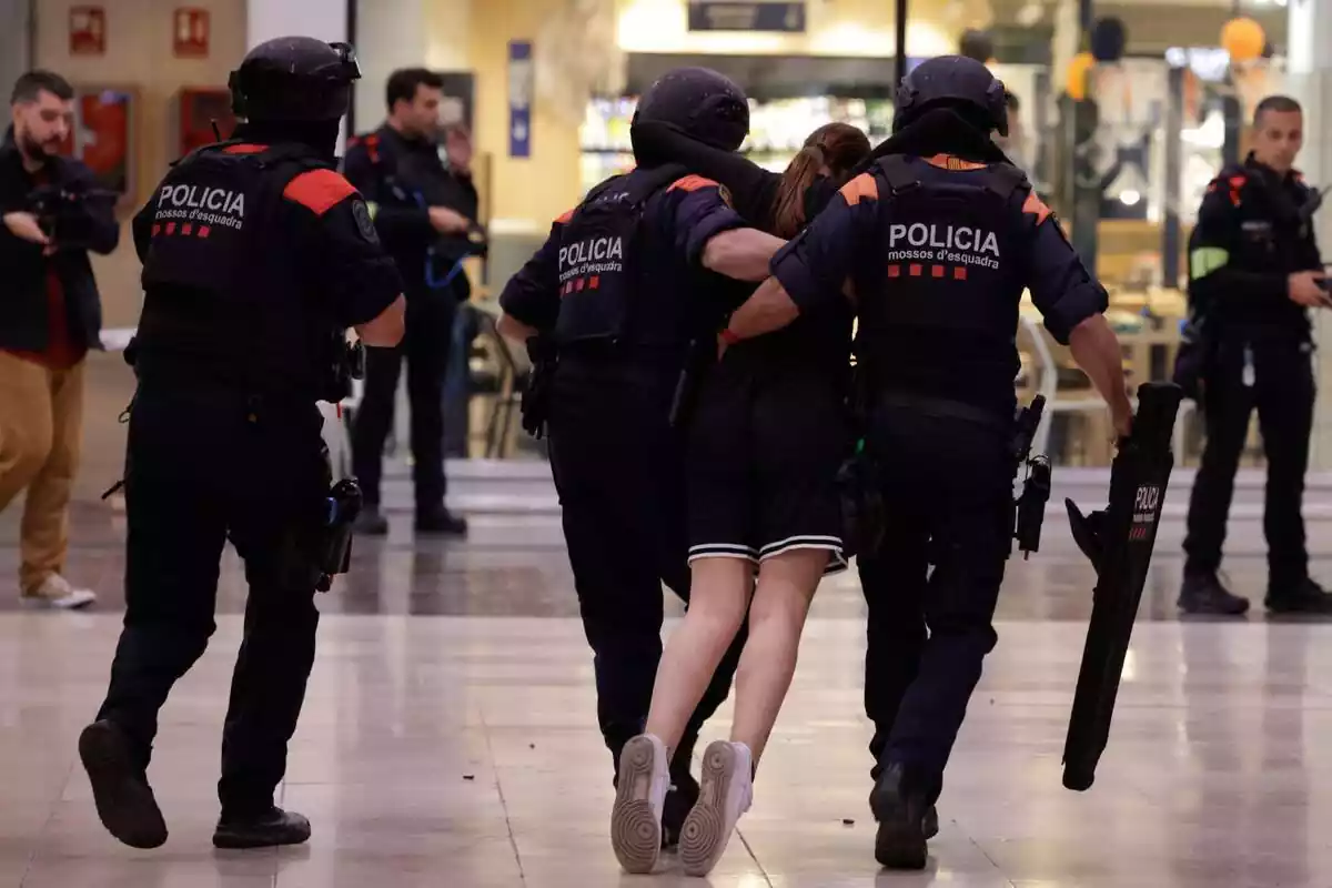 Tres Mossos d'Esquadra de espaldas, dos de ellos cogiendo a una joven que se hace la herida en el simulacro antiterrorista hecho en la estación de Sants