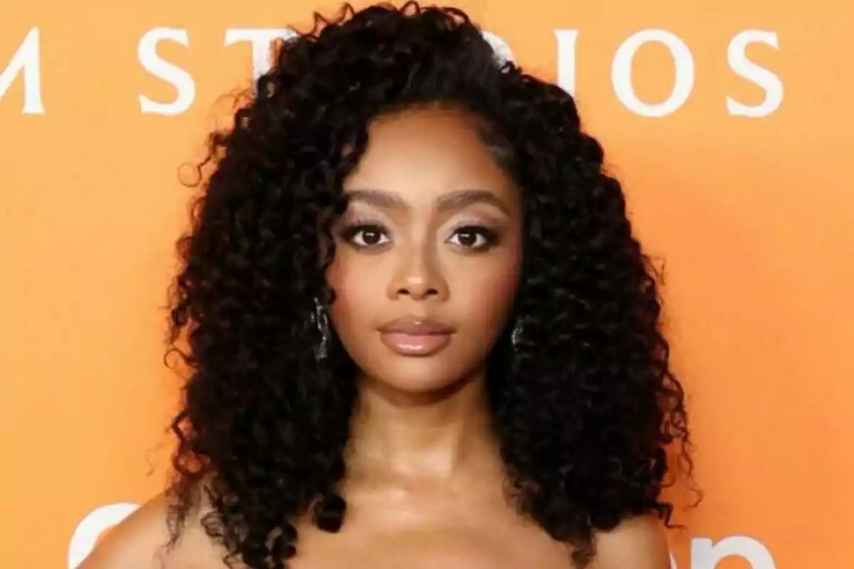 Captura de Skai Jackson con cabello rizado y vestido sin tirantes frente a un fondo naranja.