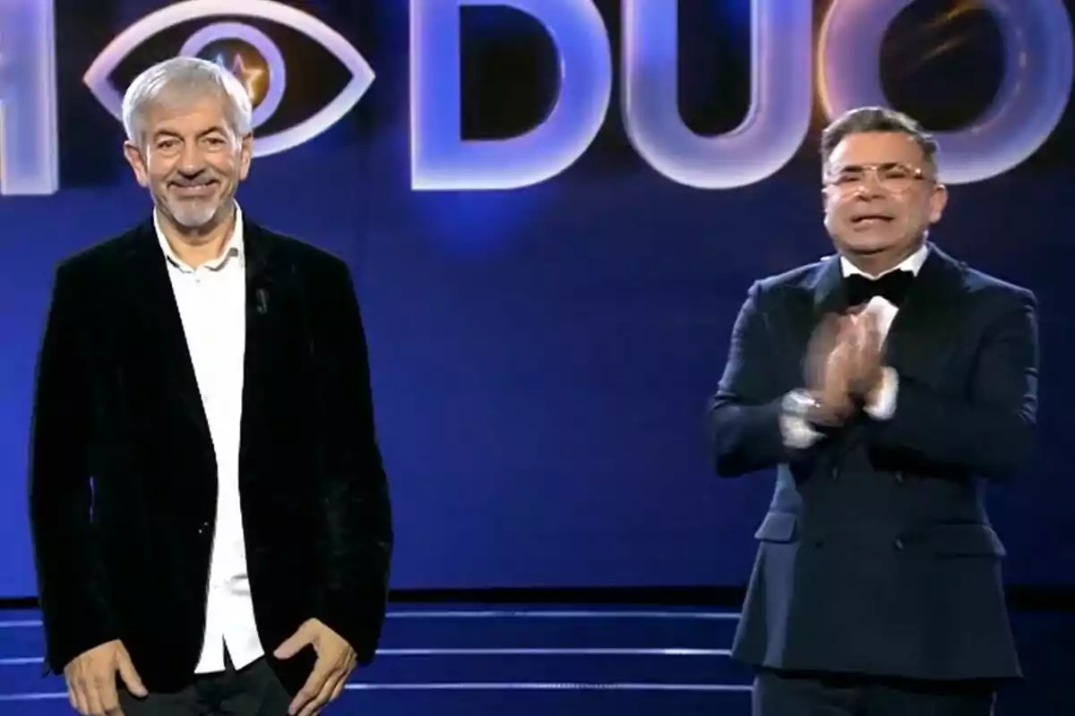 Carlos Sobera y Jorge Javier Vázquez de pie en un escenario con un fondo azul y letras grandes iluminadas de GH DÚO.