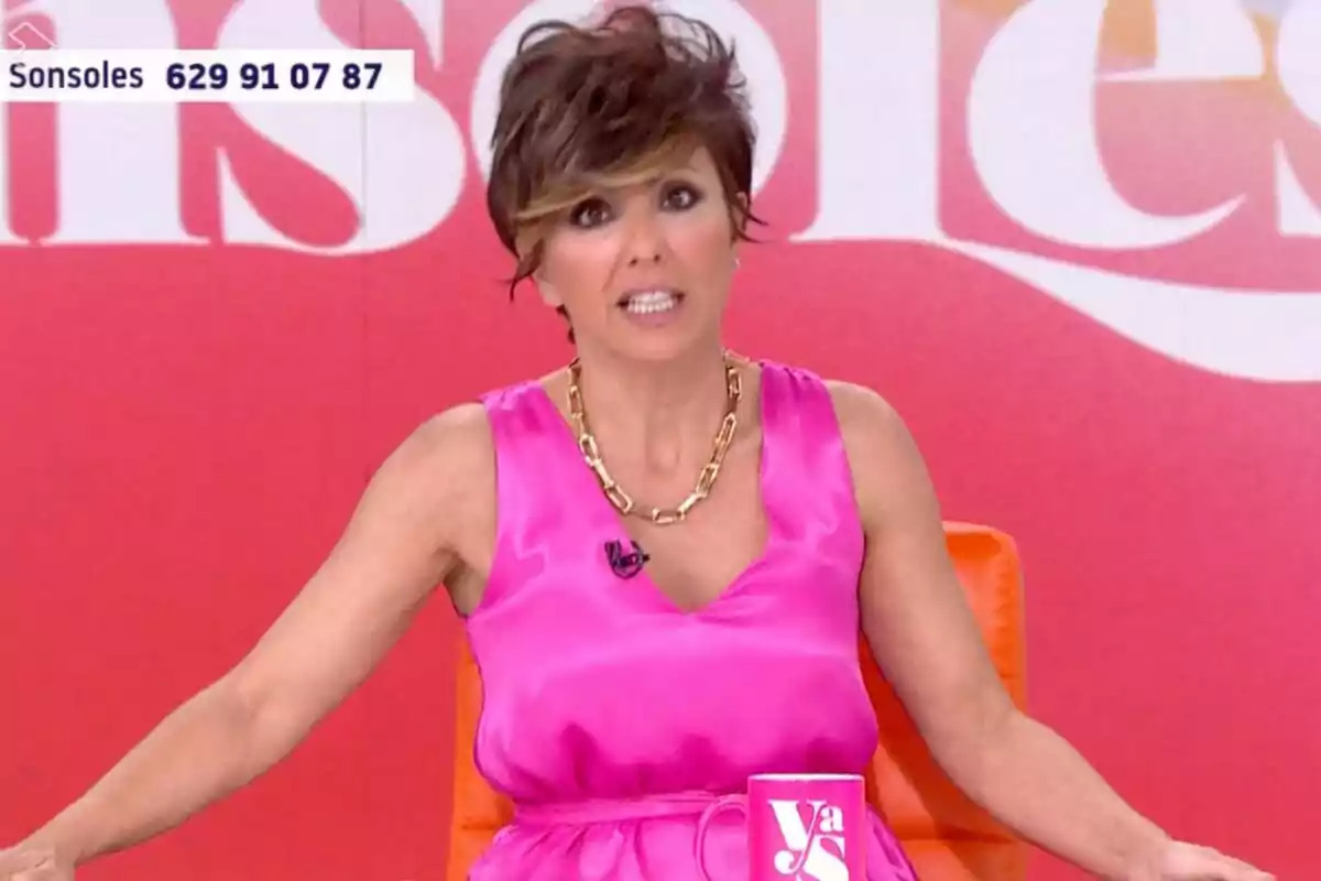 Sonsoles Ónega con vestido rosa y collar dorado sentada en 'Y ahora Sonsoles' con fondo rojo y una taza rosa sobre la mesa