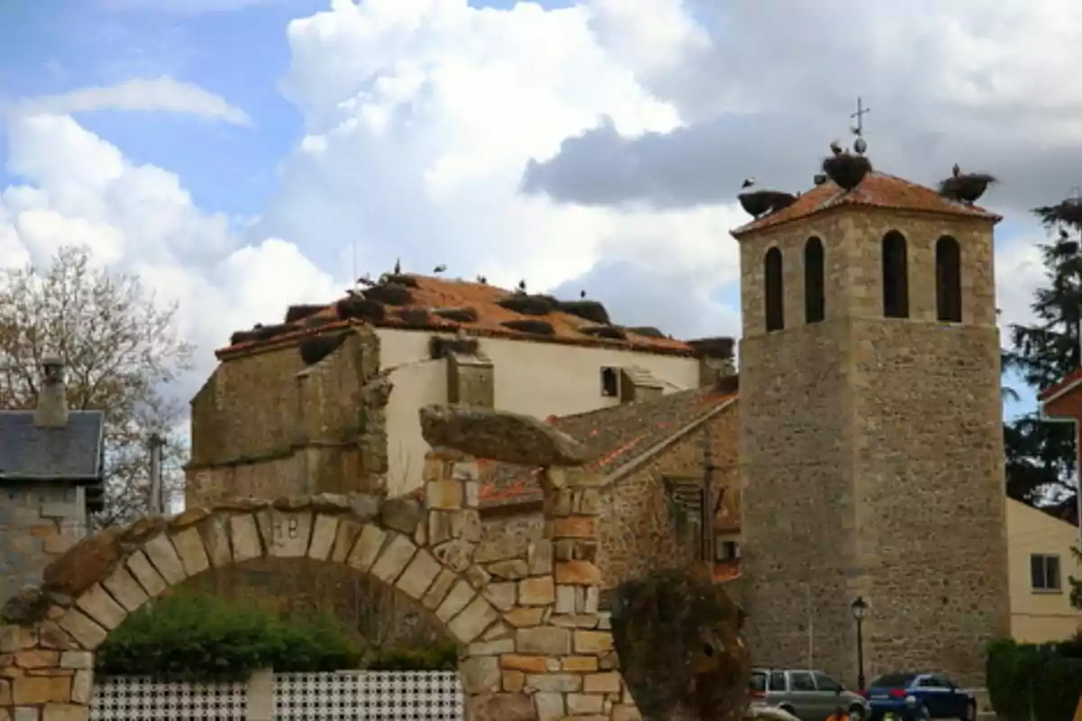 Una iglesia de piedra con un campanario y varias cigüeñas anidando en el techo bajo un cielo parcialmente nublado. Una iglesia de piedra con un campanario y varias cigüeñas anidando en el techo bajo un cielo parcialmente nublado.