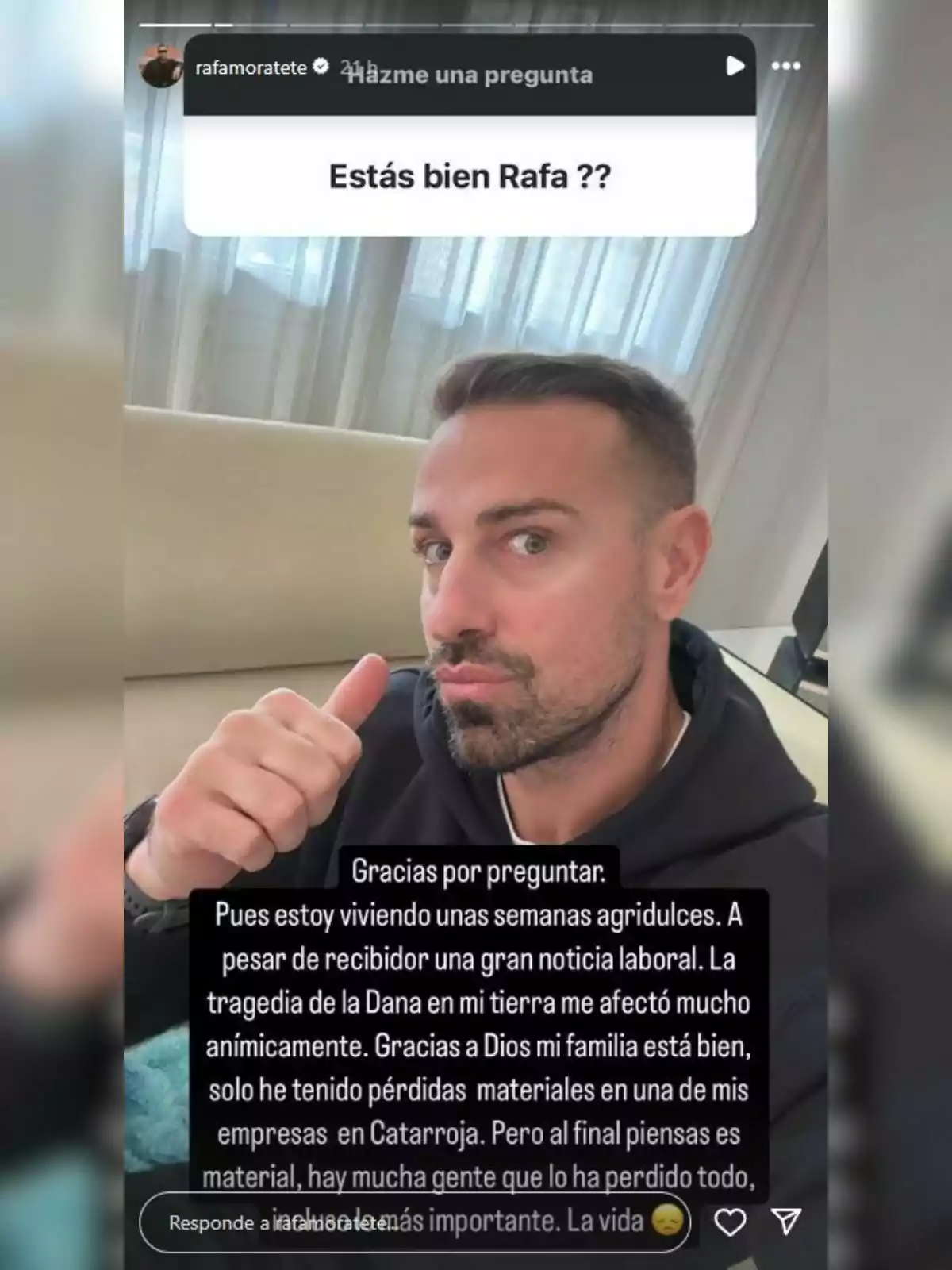 Rafa Mora con barba y cabello corto está sentado en un sofá, levantando el pulgar. Lleva una sudadera oscura y detrás de él hay una cortina blanca. En la imagen se muestra una pregunta sobre su bienestar y una respuesta agradeciendo la preocupación, mencionando que ha tenido semanas agridulces debido a una tragedia en su tierra, pero que su familia está bien.