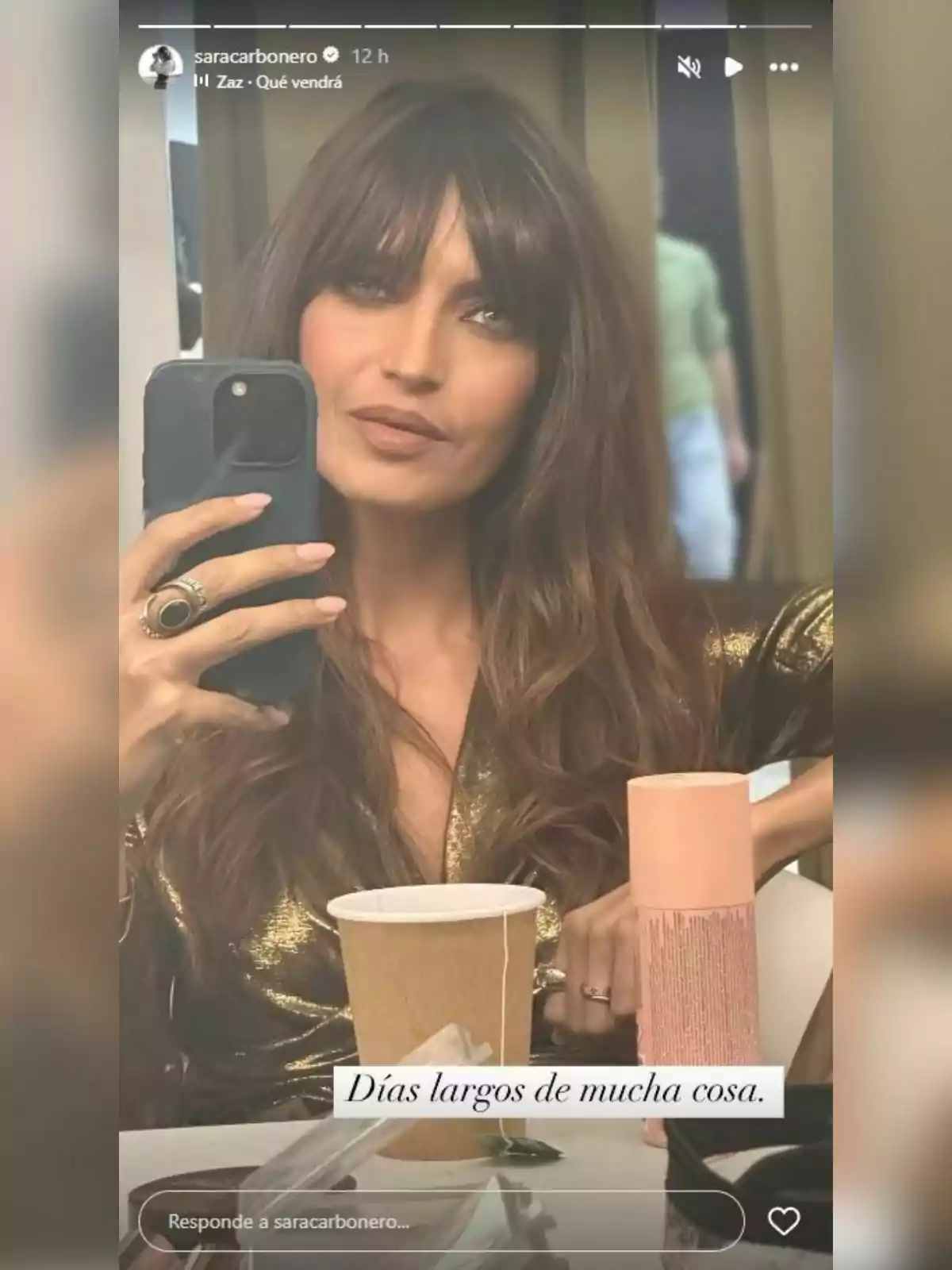 Sara Carbonero con cabello largo y flequillo se toma una selfie frente a un espejo, lleva una prenda brillante y en la mesa hay un vaso de cartón y un envase cilíndrico. Sara Carbonero con cabello largo y flequillo se toma una selfie frente a un espejo, lleva una prenda brillante y en la mesa hay un vaso de cartón y un envase cilíndrico.