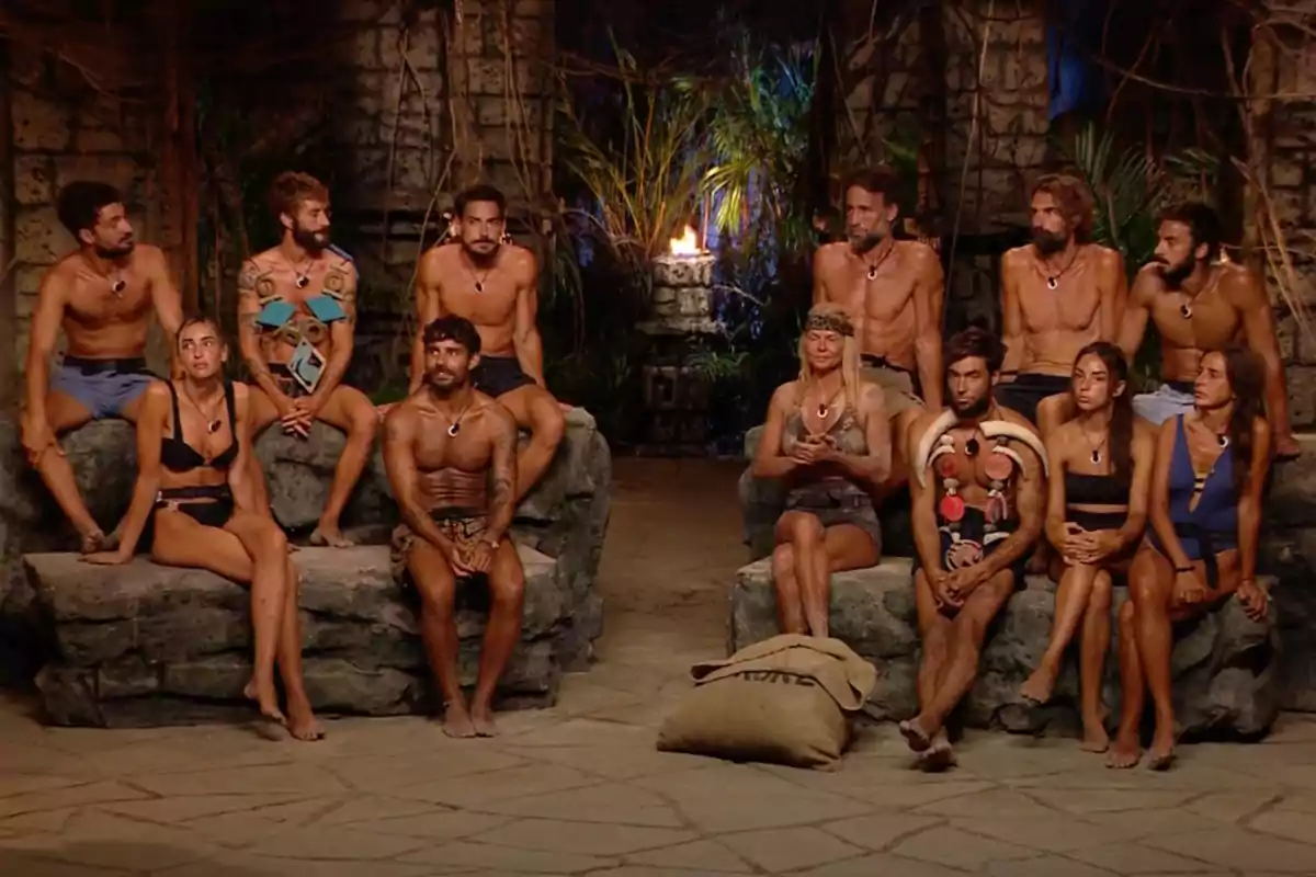 Un grupo de personas sentadas en un entorno de estilo tribal con una antorcha encendida al fondo. Captura de 'Supervivientes'