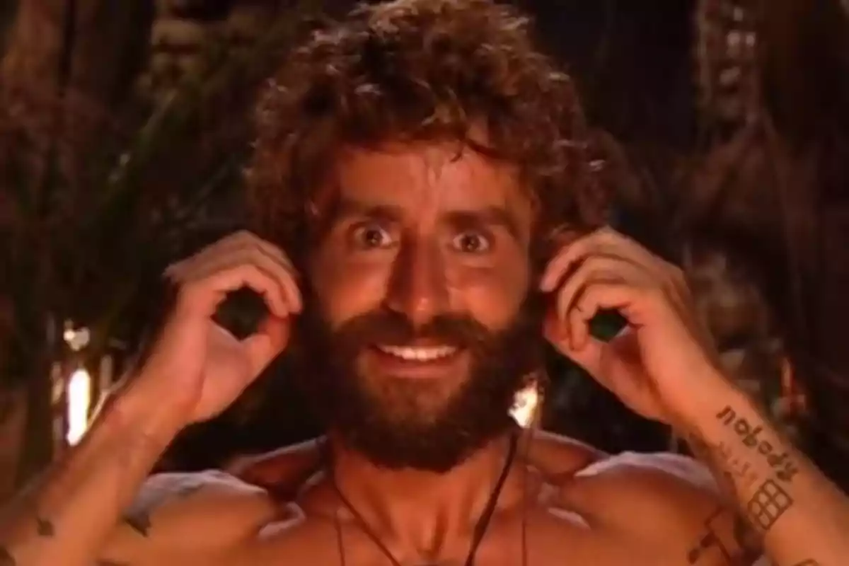 Pelayo Díaz sonríe mientras se toca las orejas con ambas manos en un entorno al aire libre iluminado por fuego. Captura de 'Supervivientes' Pelayo Díaz sonríe mientras se toca las orejas con ambas manos en un entorno al aire libre iluminado por fuego. Captura de 'Supervivientes'