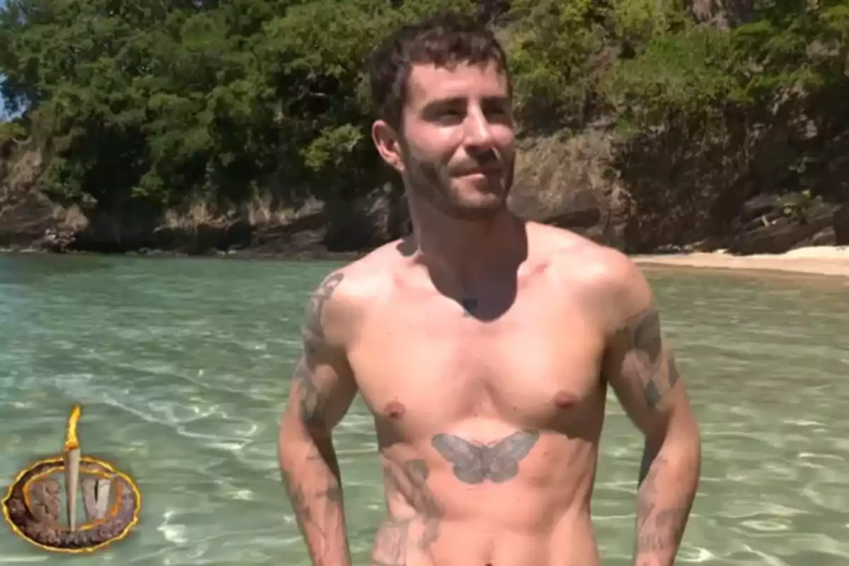 Pelayo Díaz con tatuajes en el torso está de pie en el agua clara de una playa con vegetación en el fondo. Captura de 'Supervivientes' Pelayo Díaz con tatuajes en el torso está de pie en el agua clara de una playa con vegetación en el fondo. Captura de 'Supervivientes'