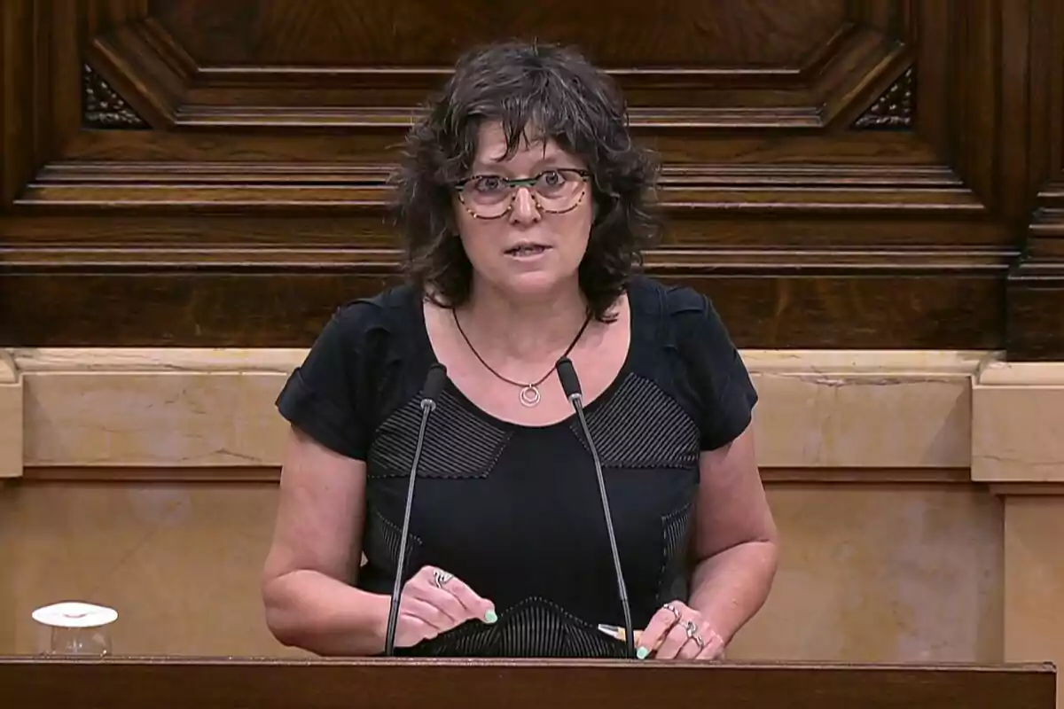 Mujer de cabello rizado y gafas hablando en un podio con fondo de madera Mujer de cabello rizado y gafas hablando en un podio con fondo de madera