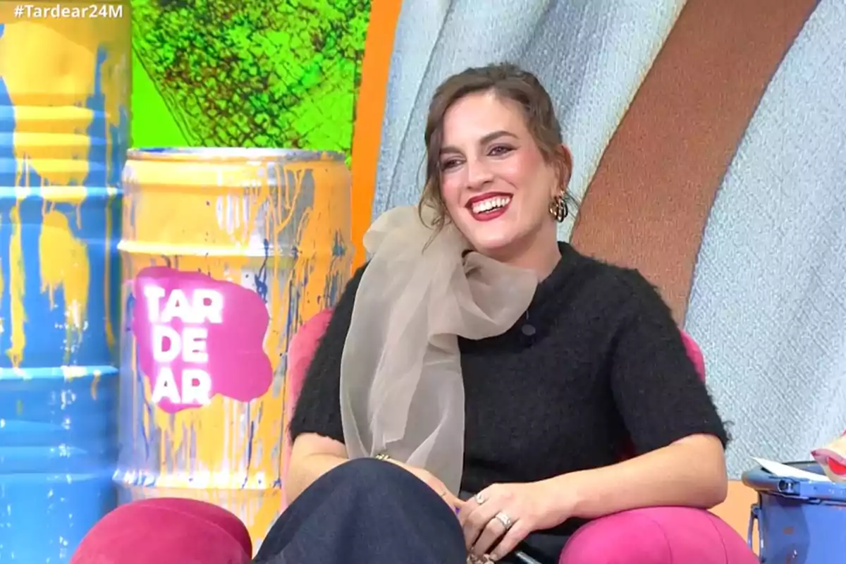 Leticia Requejo sonriente está sentada en un sillón rosa en un set de televisión colorido con barriles pintados de amarillo y azul. Captura de 'TardeAR' Leticia Requejo sonriente está sentada en un sillón rosa en un set de televisión colorido con barriles pintados de amarillo y azul. Captura de 'TardeAR'