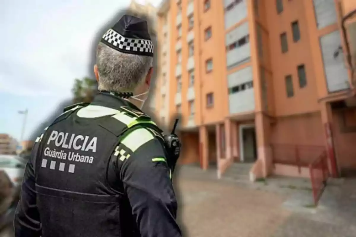 Un agente de la policía urbana de espaldas observa un edificio residencial.