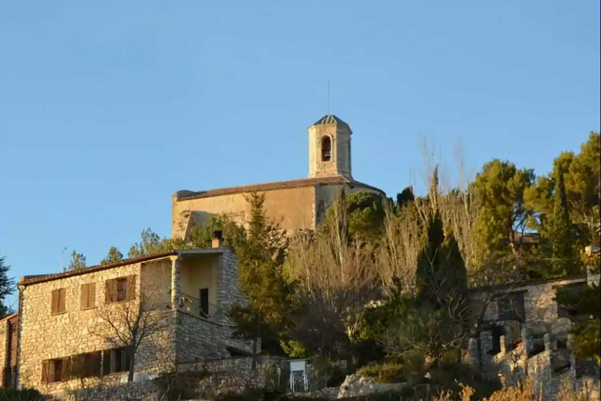 Iglesia de piedra en la cima de una colina rodeada de árboles y casas bajo un cielo despejado Iglesia de piedra en la cima de una colina rodeada de árboles y casas bajo un cielo despejado