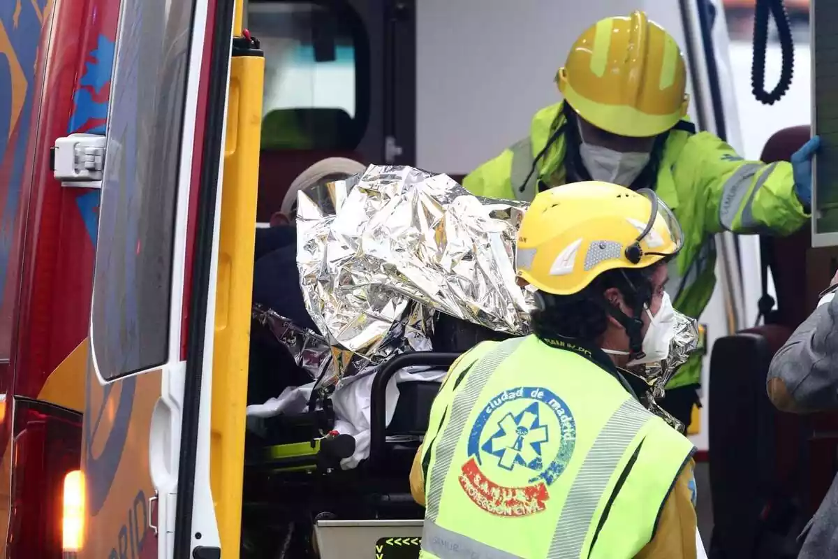 Varios trabajadores sanitarios introducen a un herido en una ambulancia en Madrid (España)