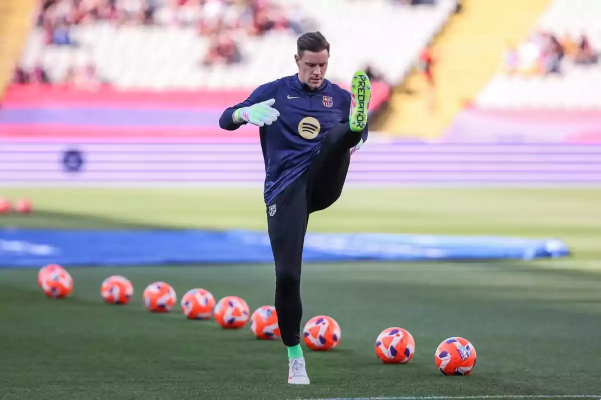 Un jugador de fútbol realiza ejercicios de calentamiento en el campo con varios balones naranjas alrededor. Un jugador de fútbol realiza ejercicios de calentamiento en el campo con varios balones naranjas alrededor.