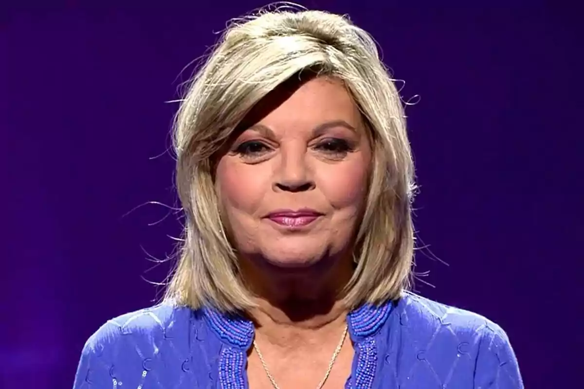 Terelu Campos con cabello rubio y expresión serena, vestida con una blusa azul, sobre un fondo morado en De Viernes.