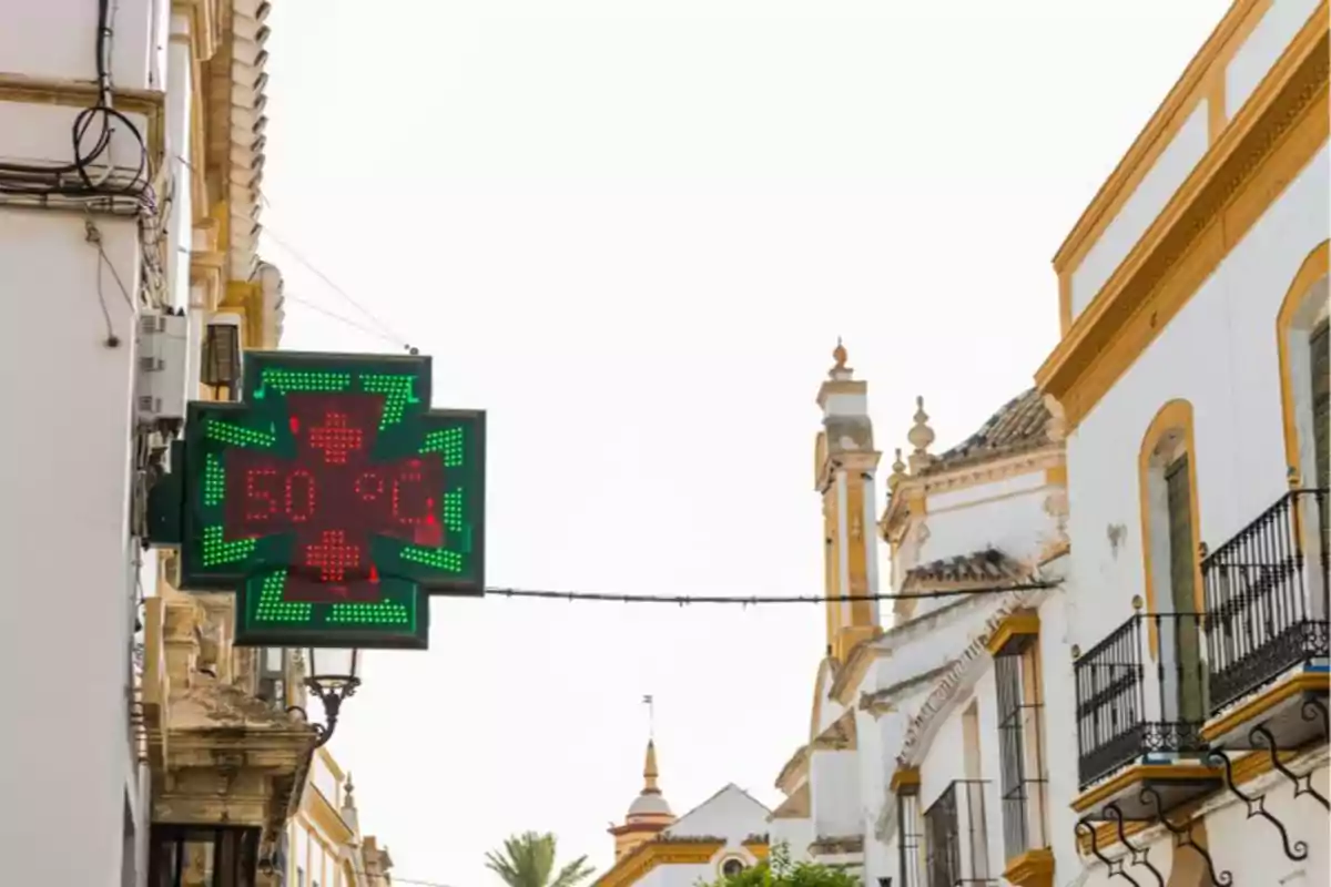 Un letrero de farmacia muestra una temperatura de 50 grados Celsius en una calle con edificios de estilo tradicional.