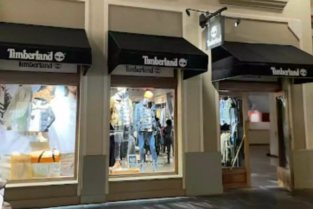Fachada de una tienda Timberland con escaparates iluminados mostrando ropa y accesorios. Fachada de una tienda Timberland con escaparates iluminados mostrando ropa y accesorios.