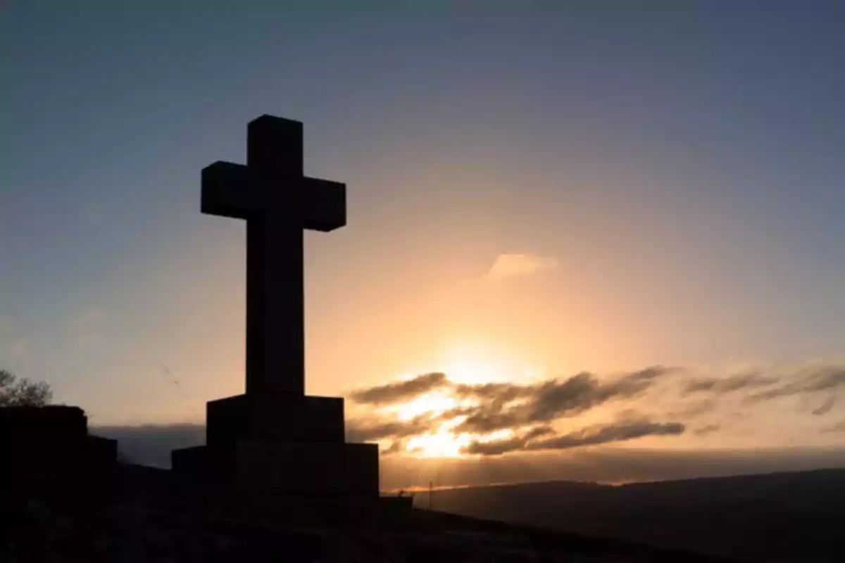 Cruz en una colina al atardecer con el cielo iluminado por el sol.