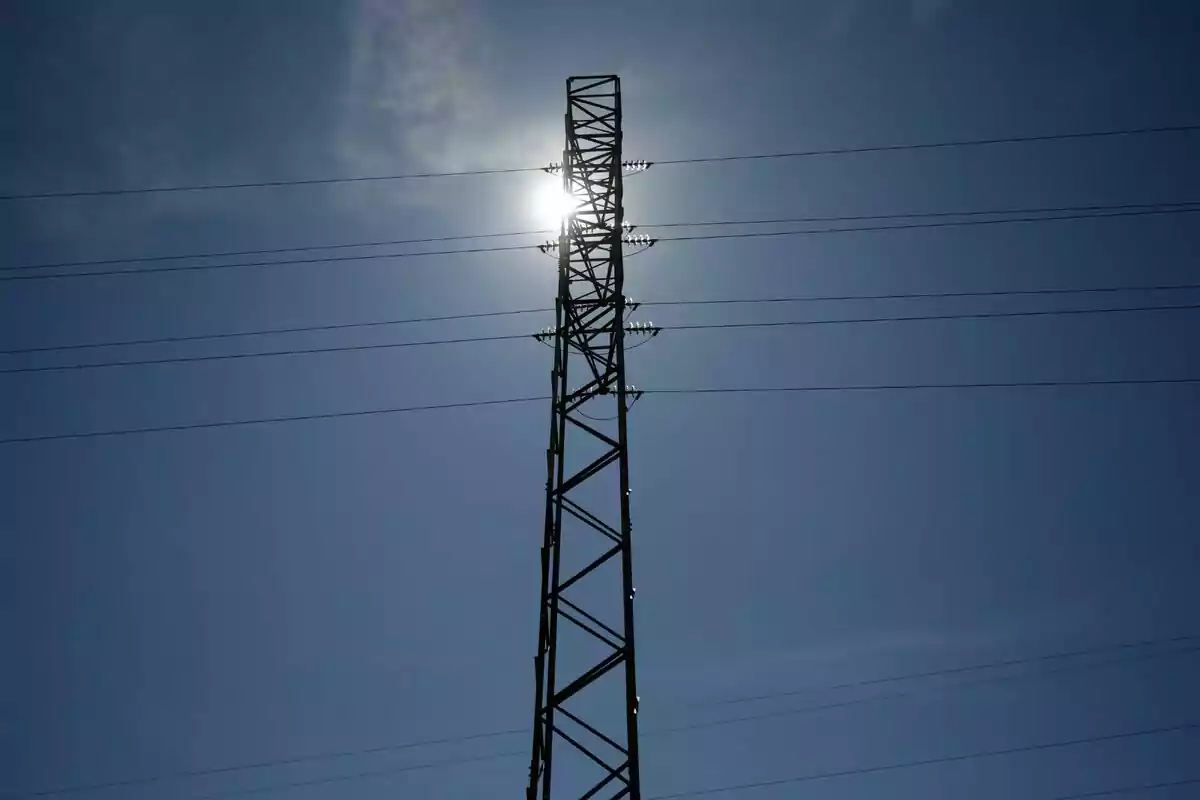 Torre de electricidad con cables y el sol brillando detrás en un cielo despejado. Torre de electricidad con cables y el sol brillando detrás en un cielo despejado.