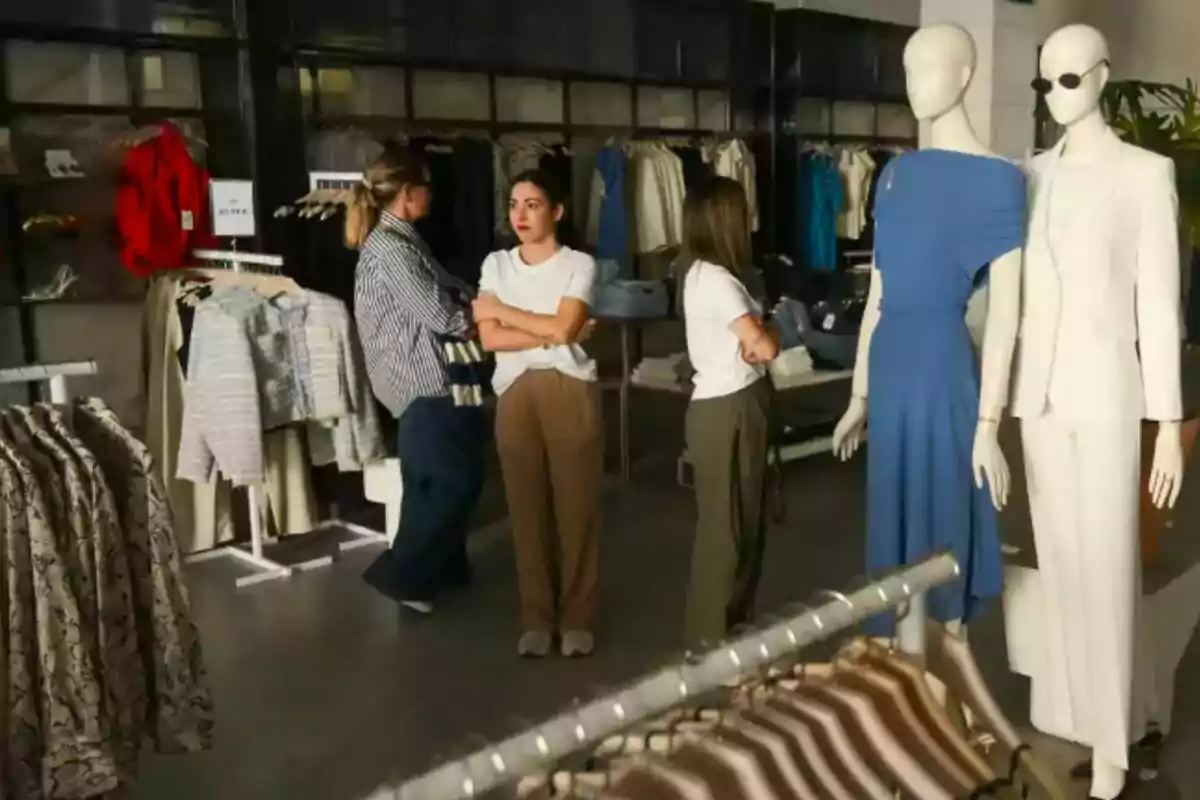 Personas observan ropa en una tienda de moda, con maniquíes vestidos al frente y percheros llenos de prendas en el fondo. Personas observan ropa en una tienda de moda, con maniquíes vestidos al frente y percheros llenos de prendas en el fondo.