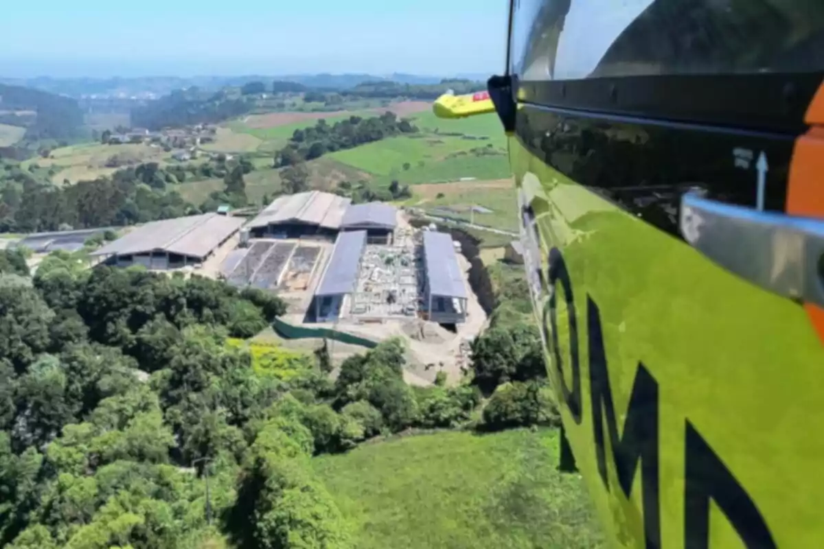 Vista aérea de una zona rural con edificios industriales y campos verdes tomada desde un helicóptero amarillo
