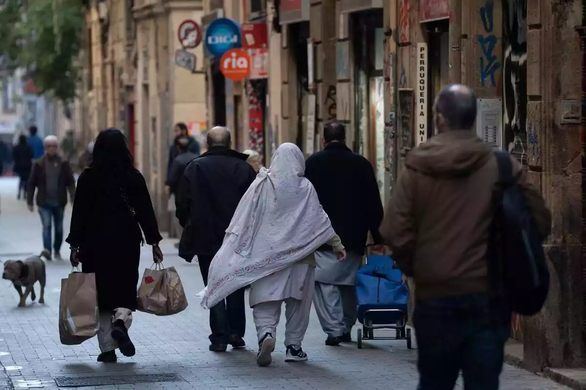 Transeúntes inmigrantes en una céntrica calle de Barcelona andando de espaldas a la cámara
